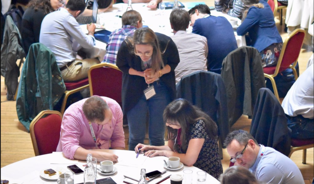 Scene from MICER, with participants discussing a research methods around tables